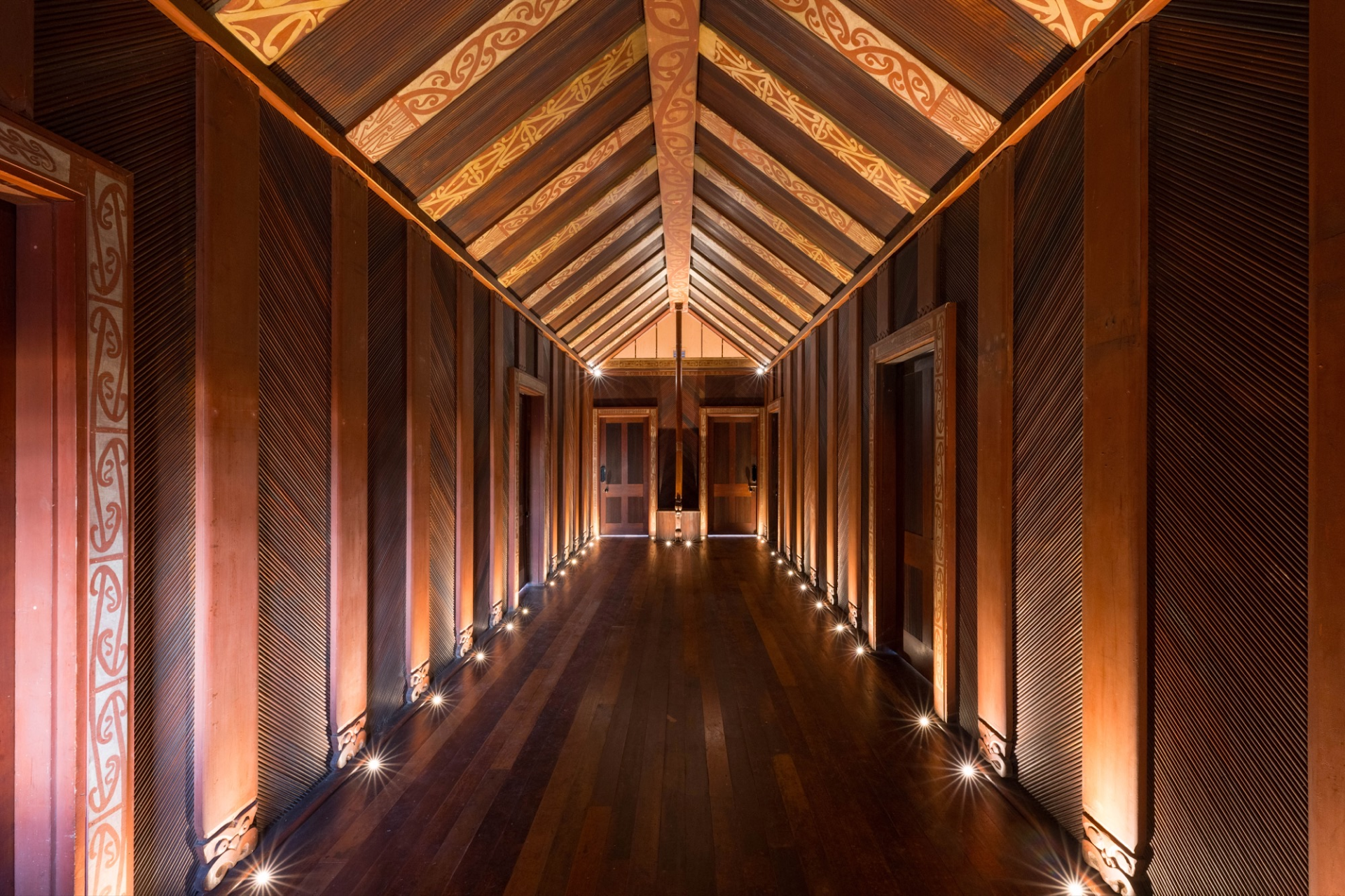 Inside the museum: fluted timber wall panels and carved doorways line the hallway, with recessed lights washing the floor.
