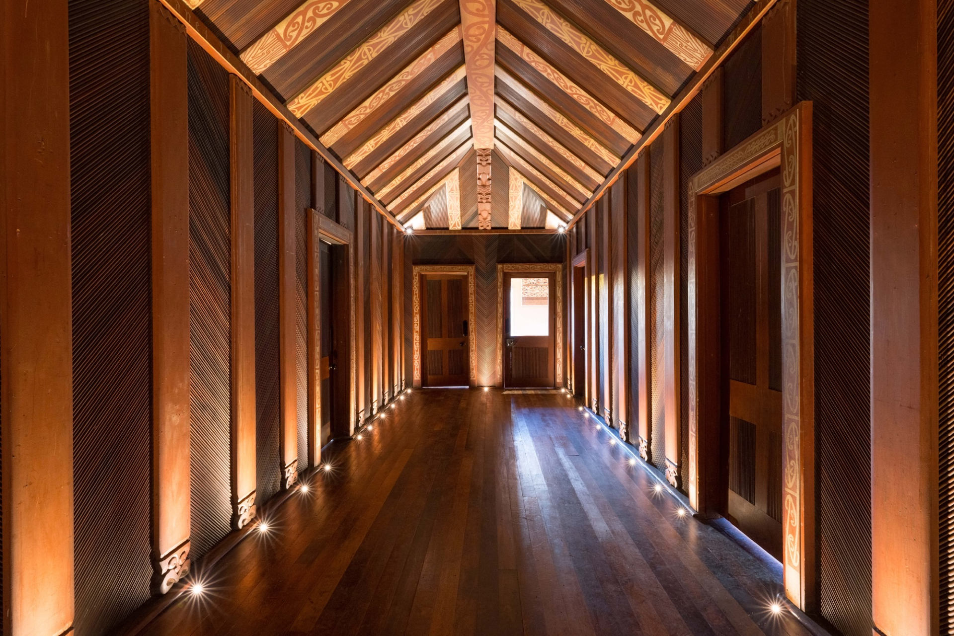 The museum's ornate hallway — a panelled corridor lit from the floor, rising to a gabled ceiling painted with kōwhaiwhai patterns.
